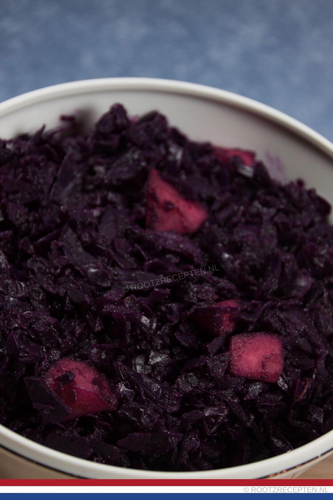 close-up van rode kool met appels in een witte schaal met een blauwe achtergrond