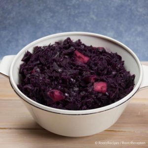 red cabbage with apples in a white serving bowl on a white wash table with a blue background